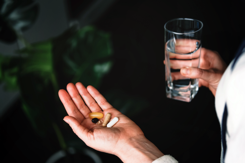 A person holding pills in one hand and with a glass of water in the other