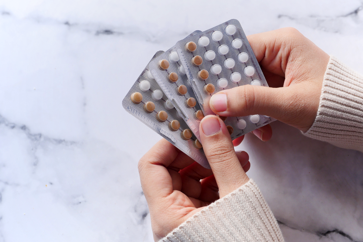 A person's hands holding three strips of pills