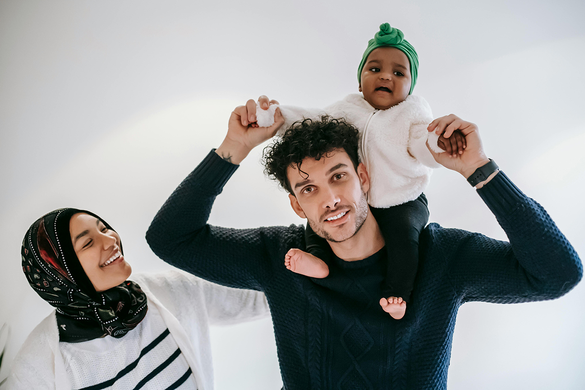 One parent carrying the child on shoulders while the other parent is supporting