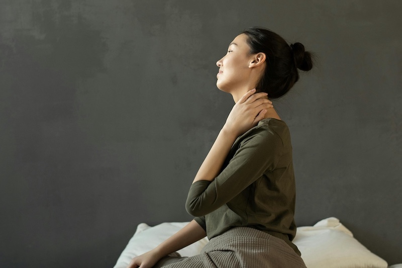 Person sitting on a bed and touching their neck