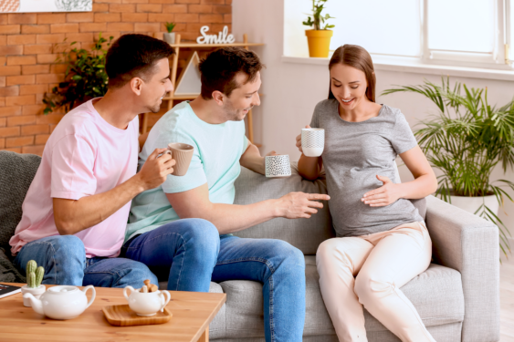 A pregnant person and a couple sitting on a couch and having coffee