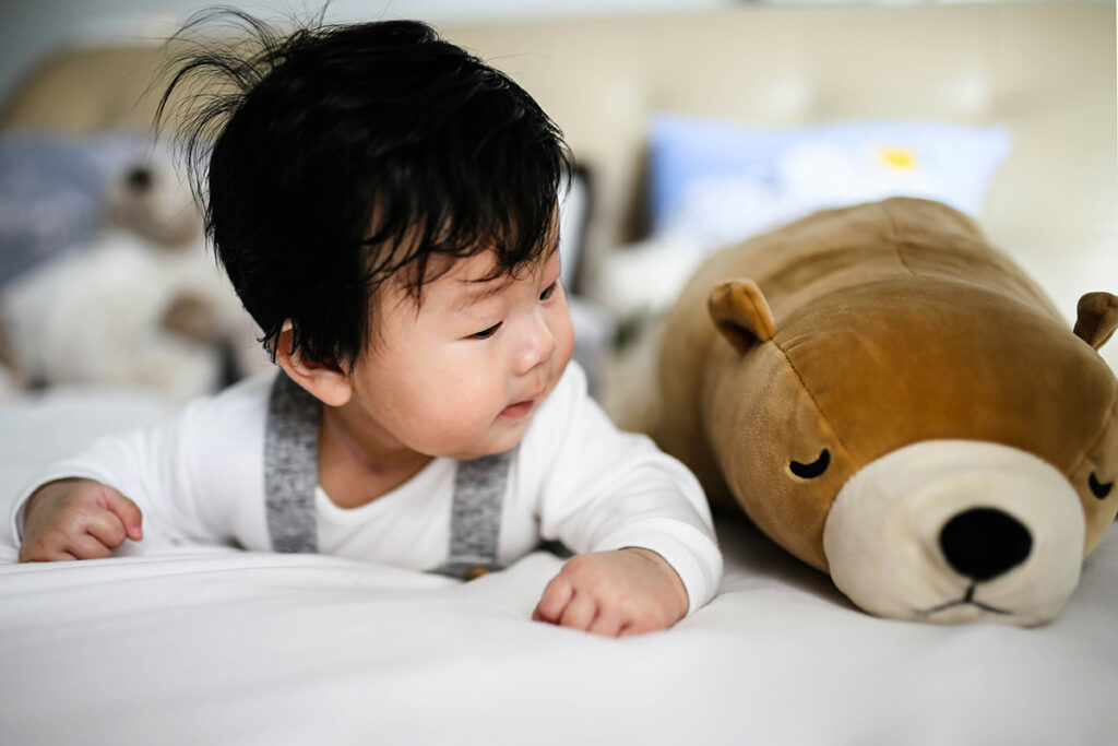 A baby lying on tummy next to a teddy