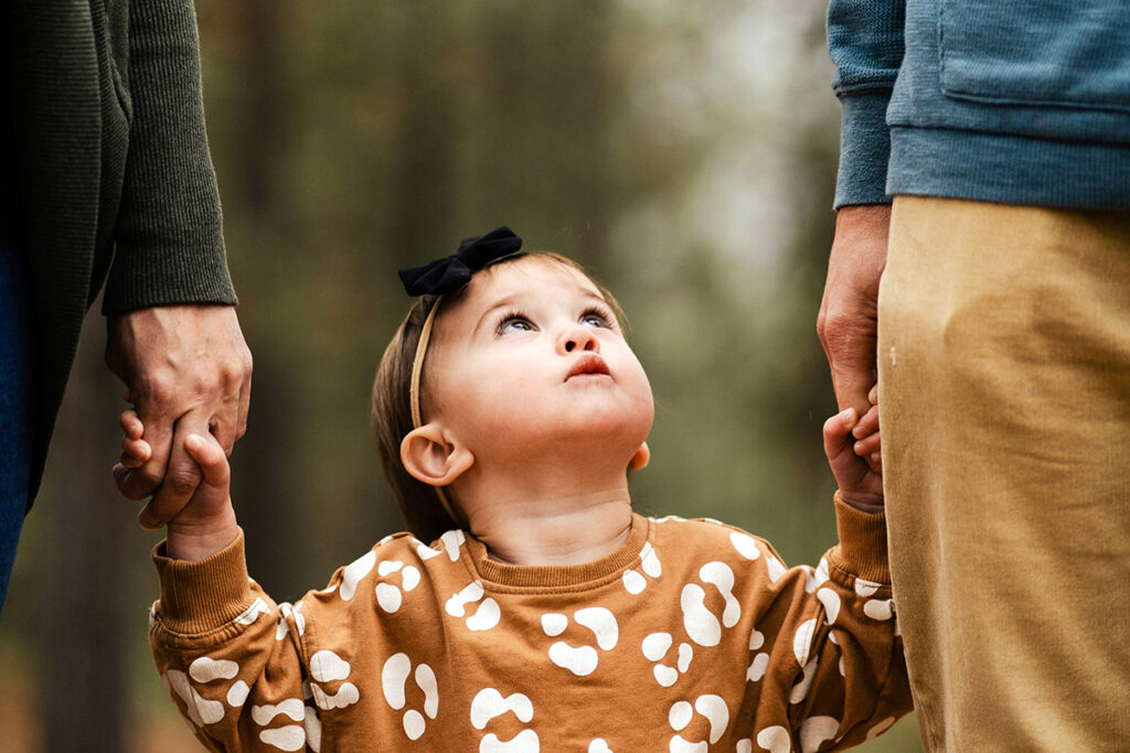 A kid holding hands of the parents and looking at them