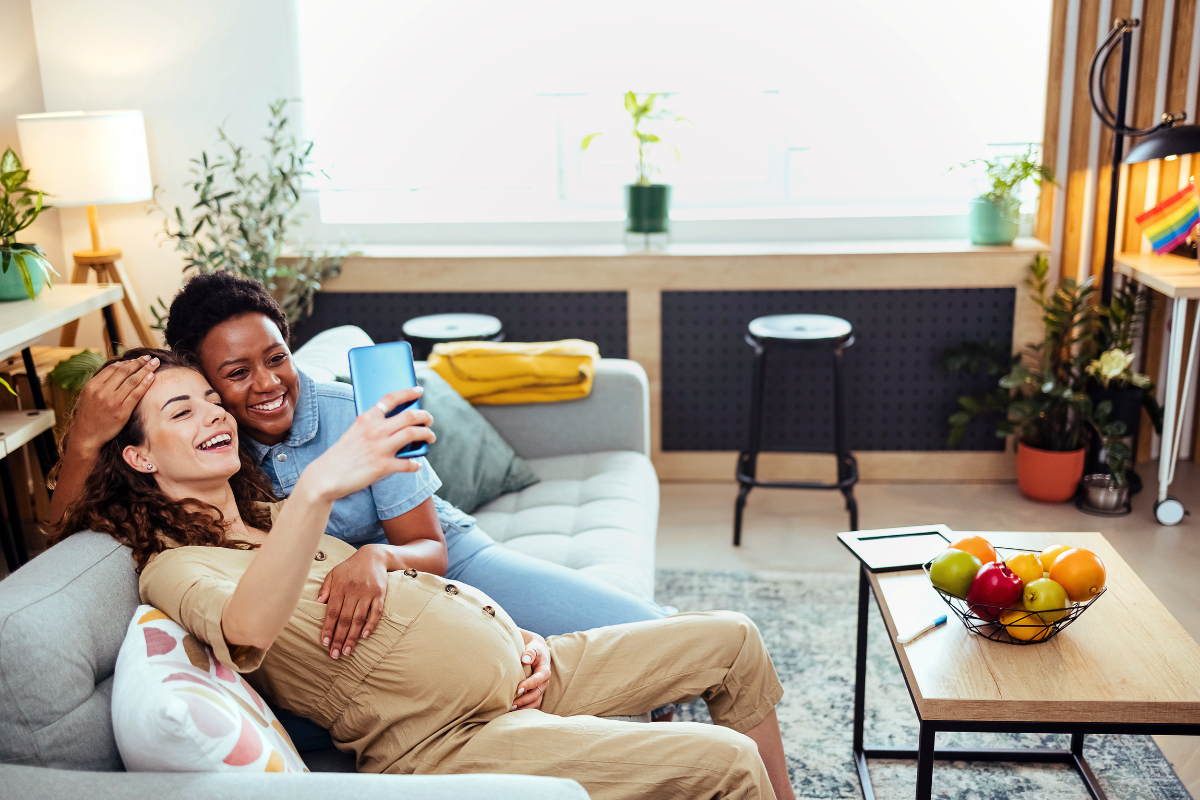 A pregnant person and another person taking a selfie on the couch