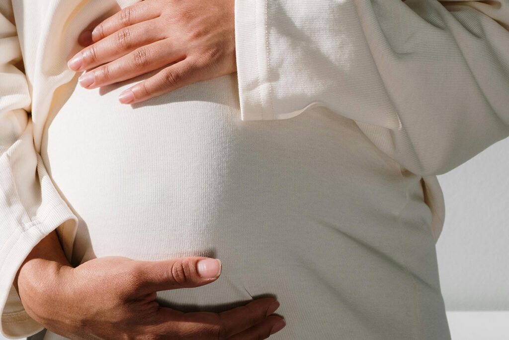 A pregnant person in white dress touching her belly