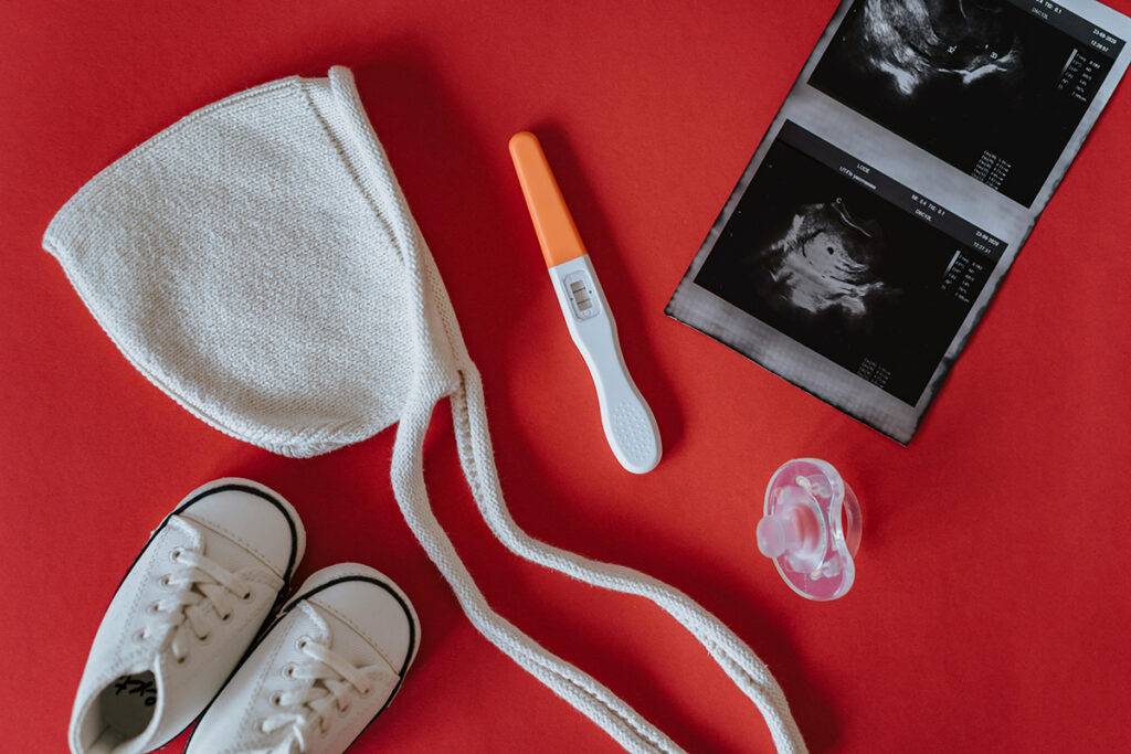 A tiny shoe, pregnancy test, Ultrasound, bib and a pacifier on a red background