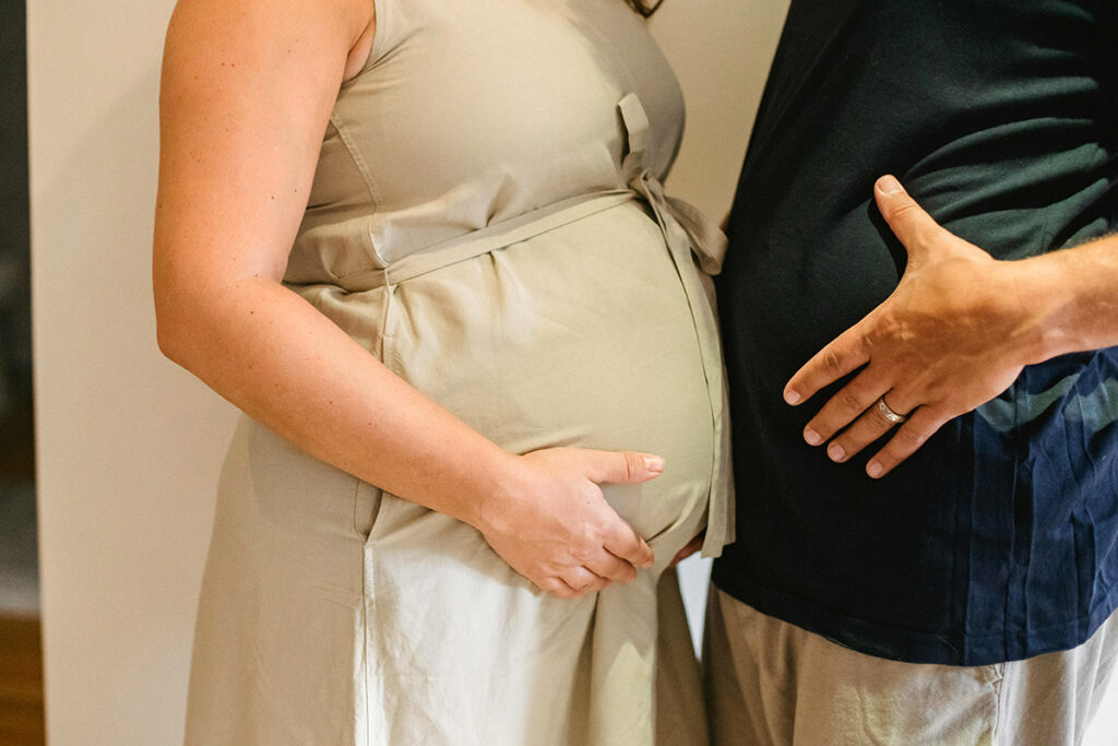 Two people holding their belly with hands , one person being pregnant