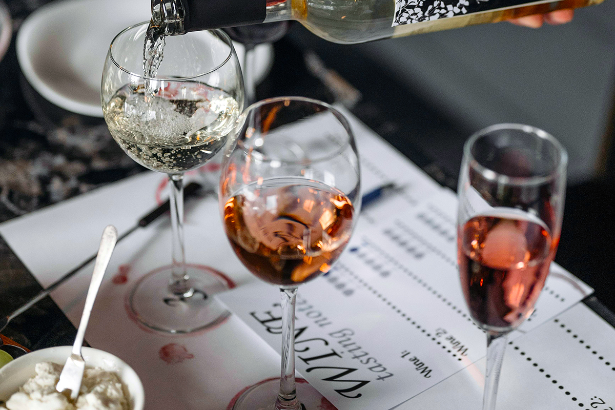 Assorted glasses of wine, on top of wine tasting sheet. Wine is being poured into the farthest left glass.