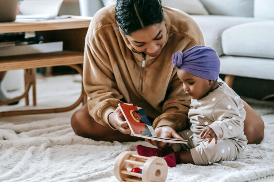 A parent and a baby sitting on a rug and reading