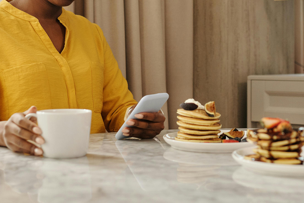 A person drinking coffee, eating pancakes and checking the phone