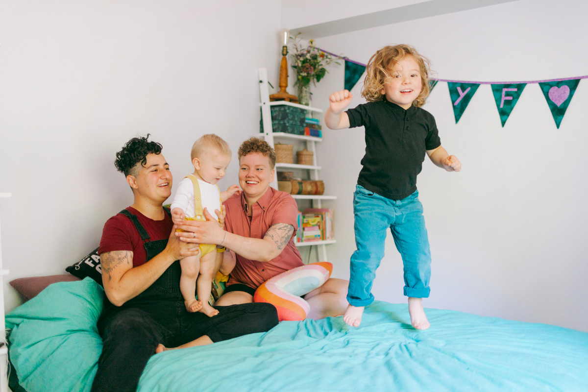 A family of parents and two kids playing on bed