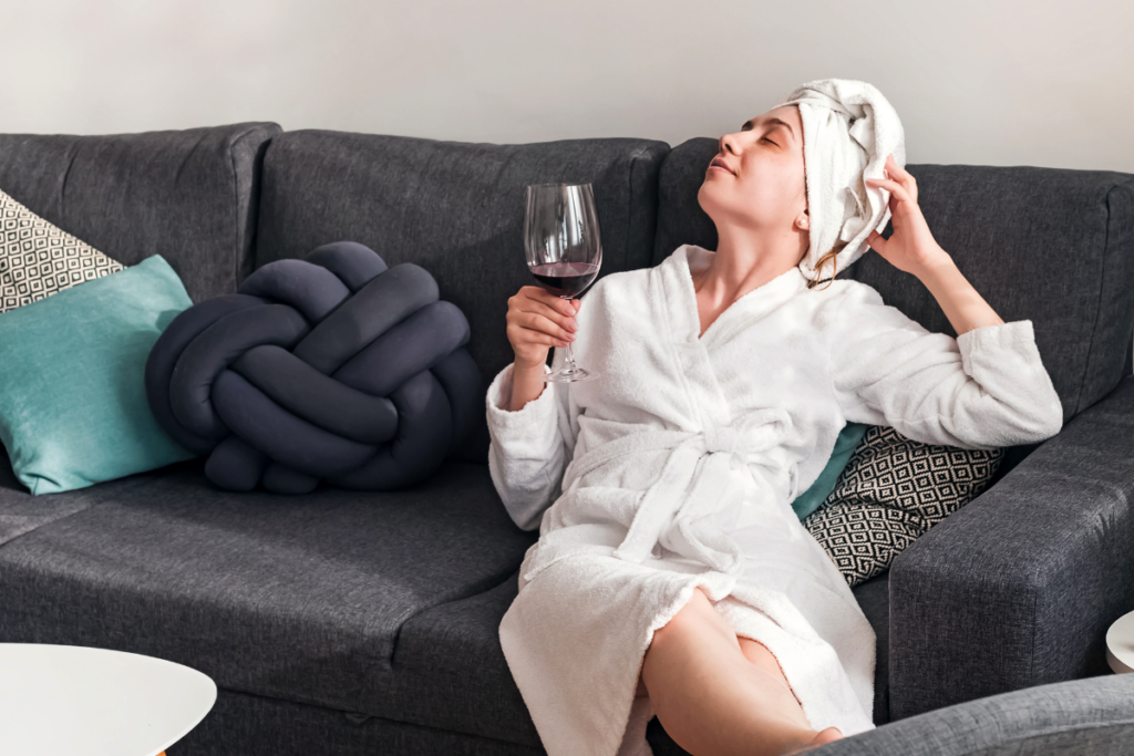 A person sitting in bath robes on a couch and enjoying a glass of wine.