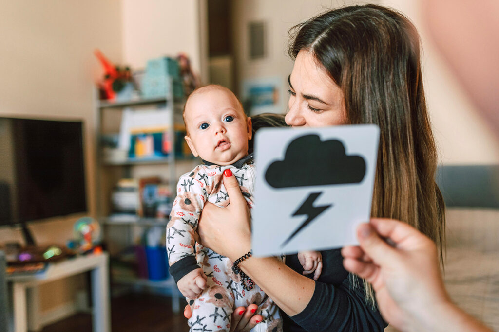 A parent holding a baby while another is showing a flash card