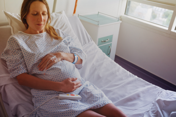 A pregnant person lying on a hospital bed and holding her pregnant belly