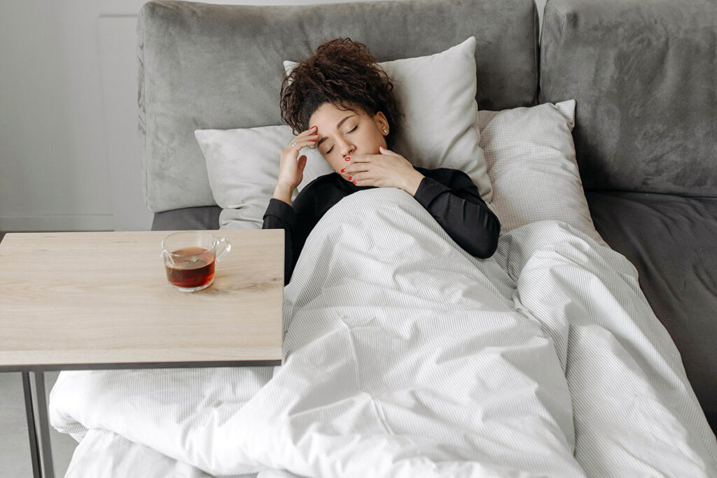 A person lying down on bed feeling nauseated with some tea by the side