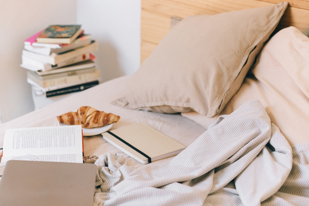 Bed with messy sheets, croissant, a laptop and books.