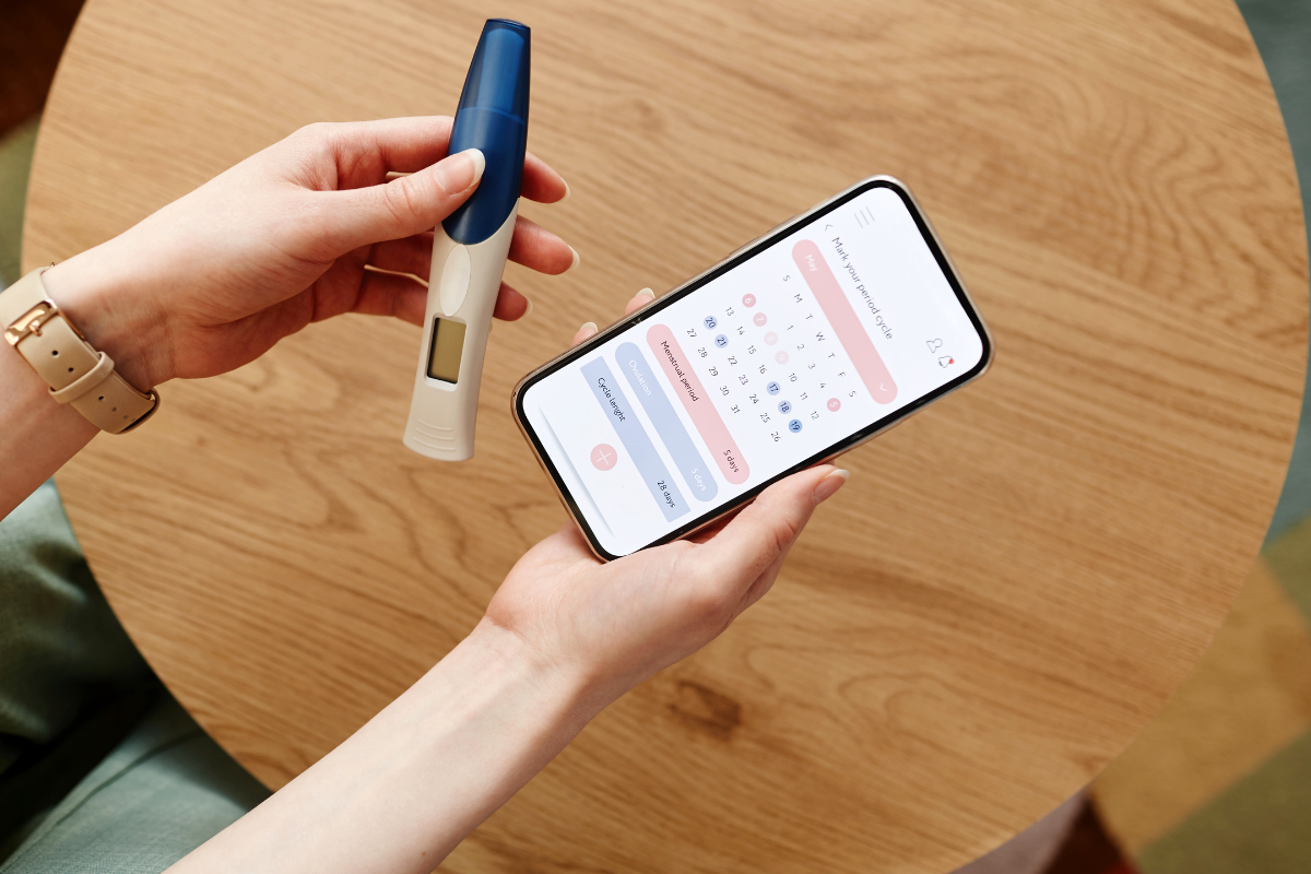 A person looking at the calendar in the phone and holding a pregnancy test.