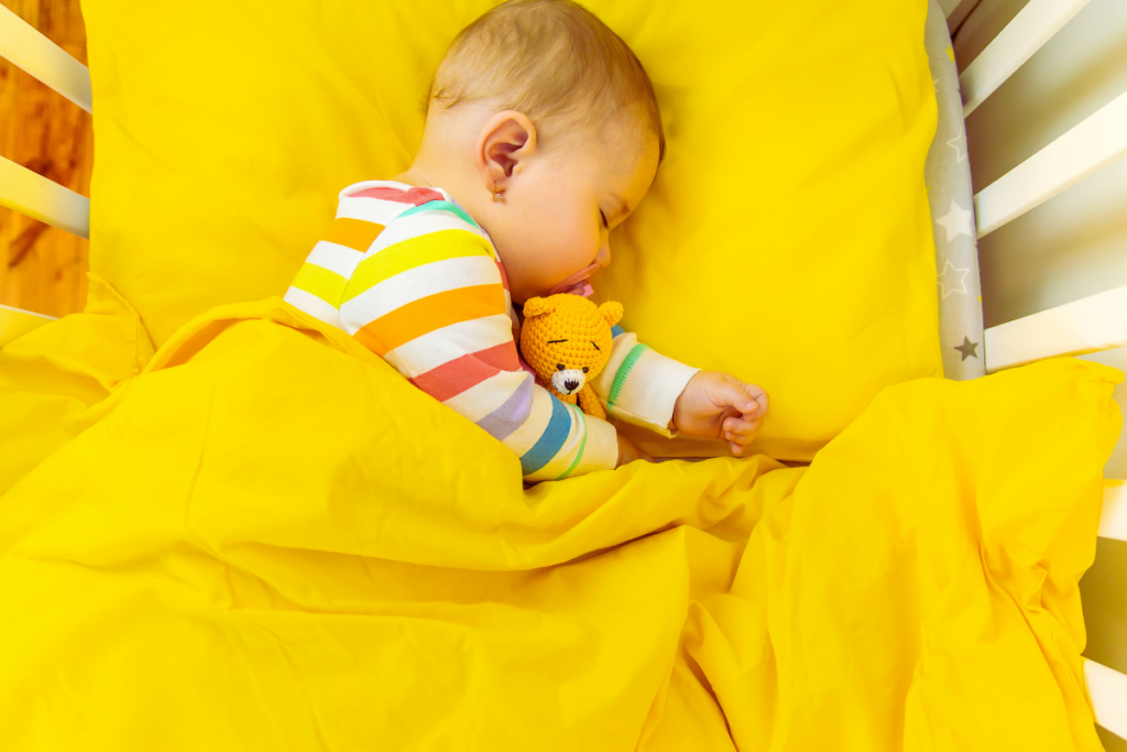 A baby sleeping in a crib with pillow and teddy.