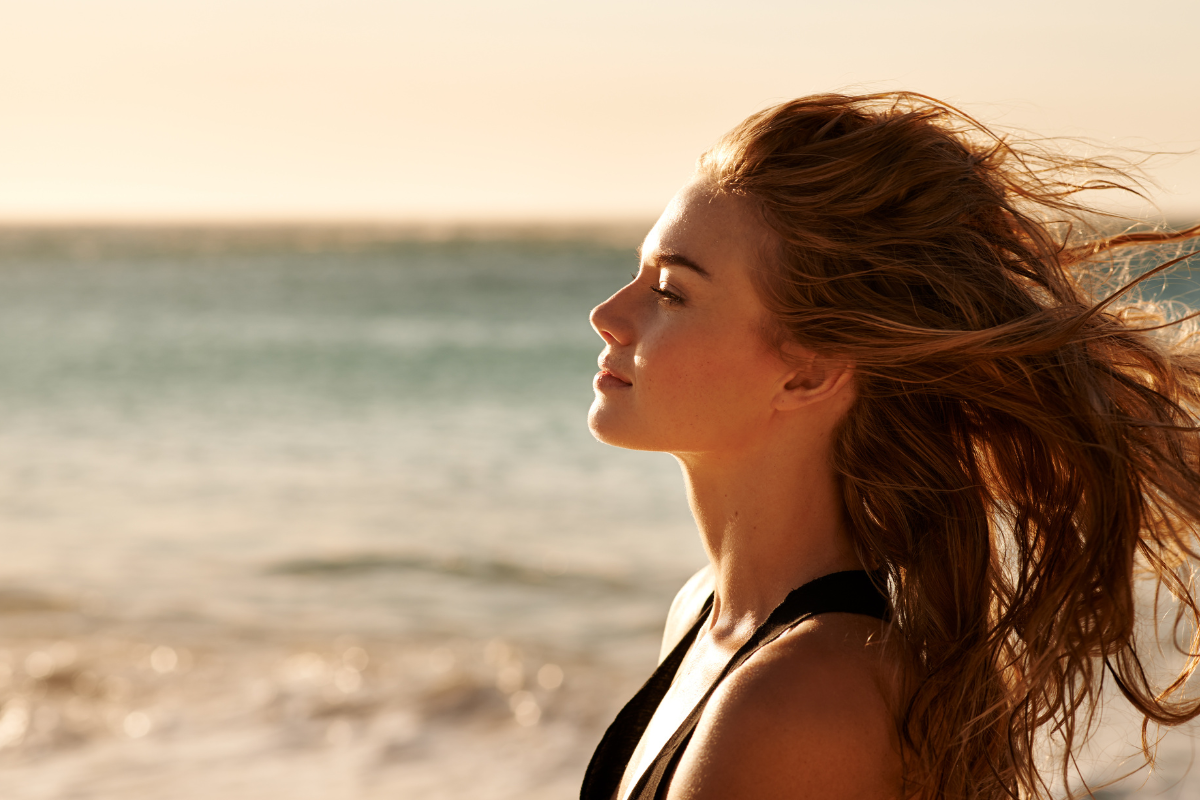 A person standing on a beach with wind on her hair