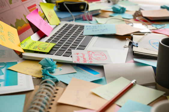 A chaotic desk with a laptop and notes.