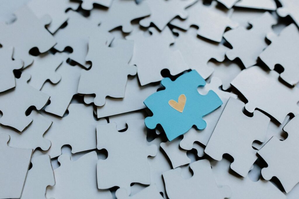 A blue puzzle piece with yellow heart on lots of grey puzzle pieces.