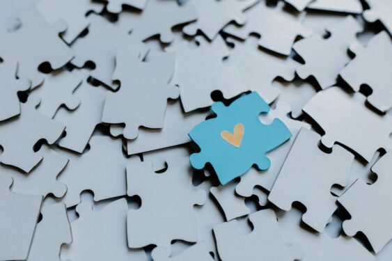 A blue puzzle piece with yellow heart on lots of grey puzzle pieces.