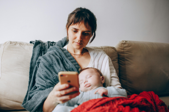 A person checking her phone while having her sleeping baby in her lap.