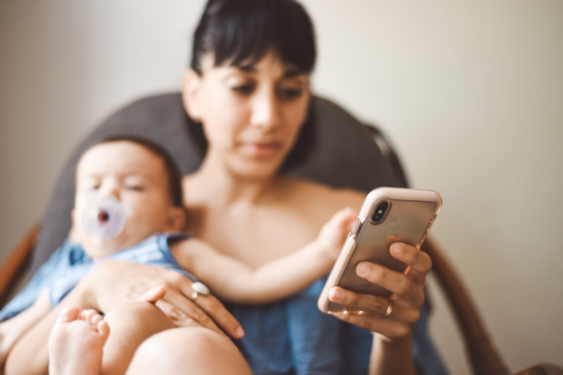 A parent looking a her phone with baby in hand.