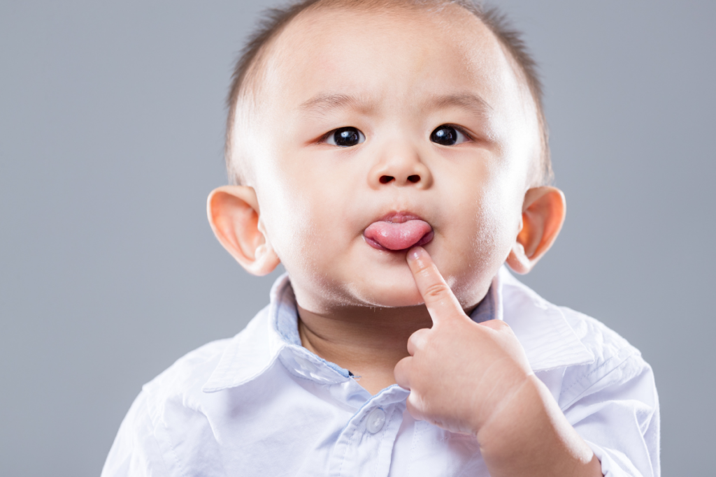 A baby sticking his tongue out and pointing at it.