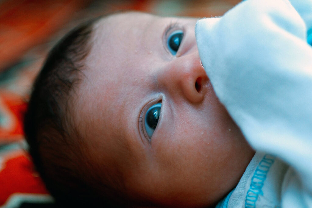 A baby lying down with a blanket covering the mouth.