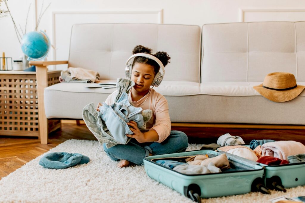 Child with headphones folding clothes and packing suitcase.