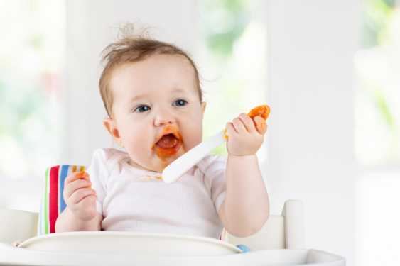 A baby in a high chair eating a puree out of spoon.
