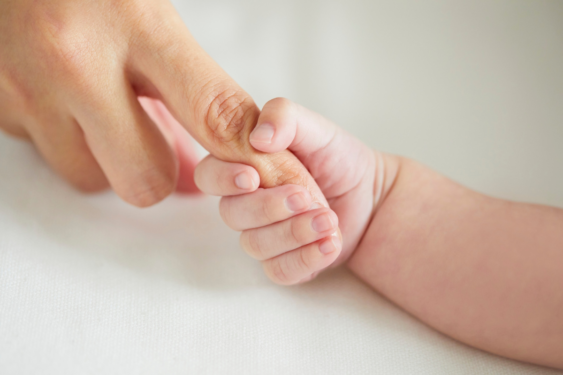 A baby holding a parent's finger.