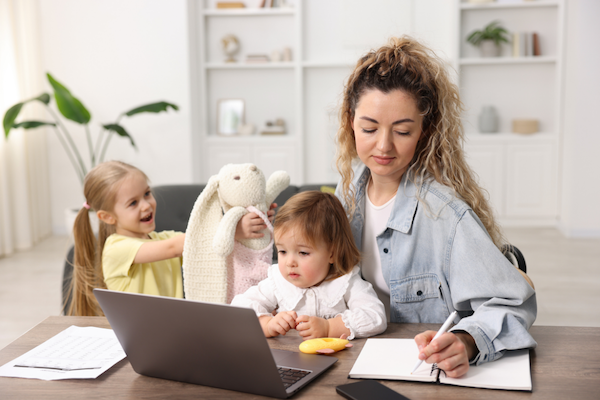 A mom working on the laptop with two children.