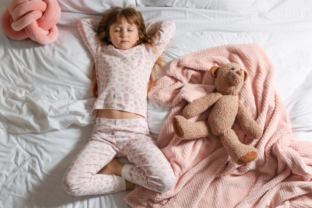 Little girl in pajamas lying on bed with eyes closed