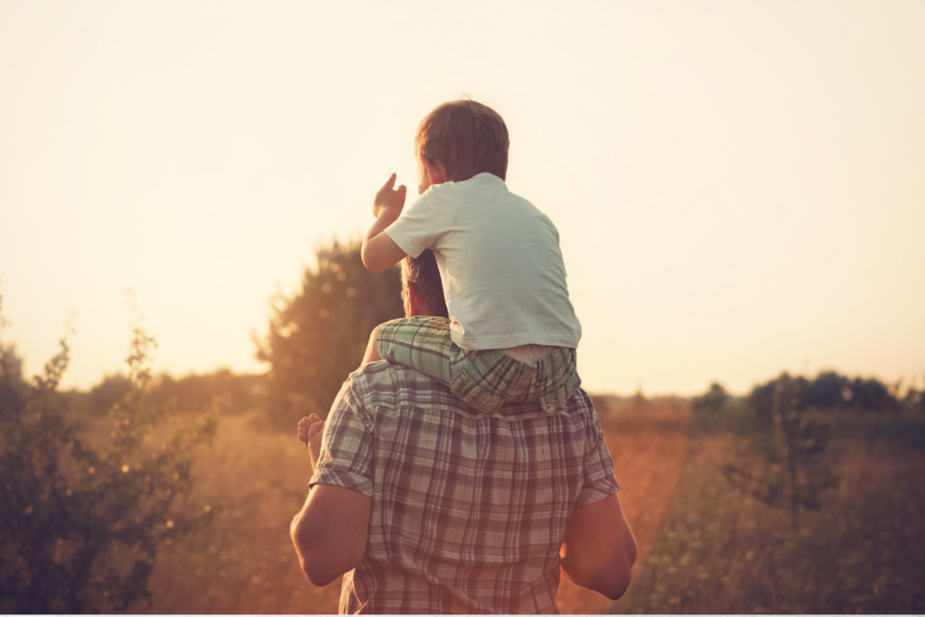 Son on dad’s shoulders in a field